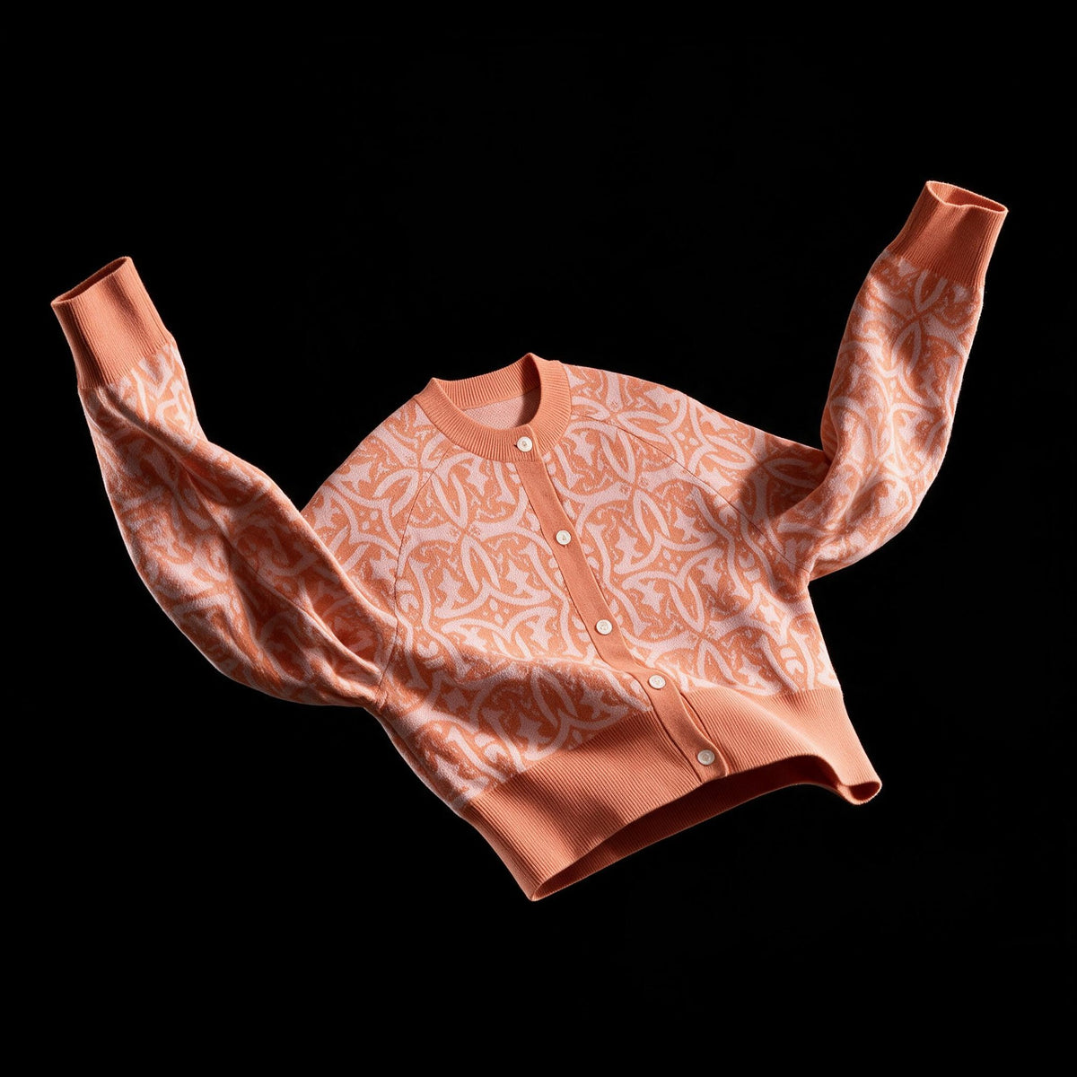 Peach and pink merino jacquard cardigan with medieval pattern, sleeves raised, on black