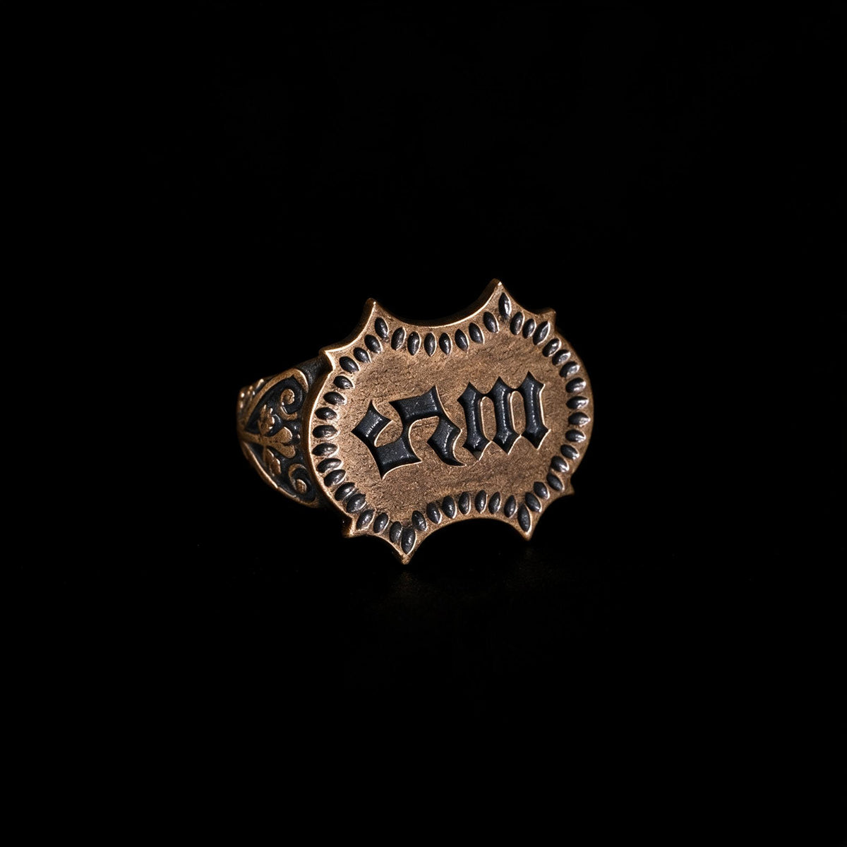 Otherworldly gothic signet ring with a pointed shield face, blackletter monogram, roped border and coppery oxidized tone