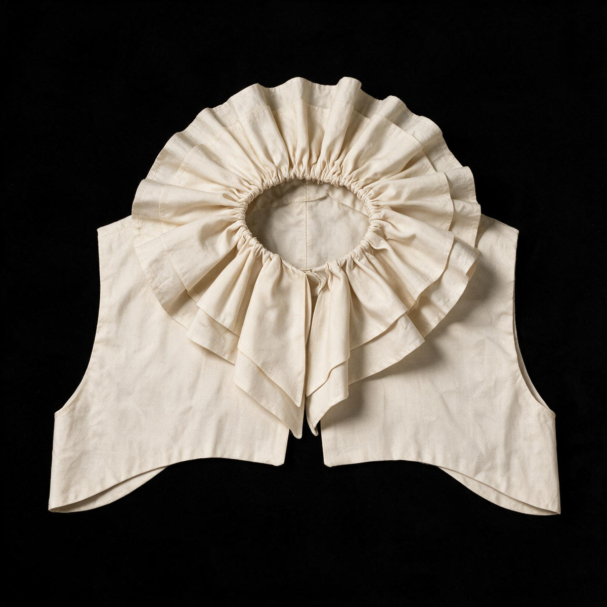 Ecru ruff collar laid flat, gathered frill circling the neck above a pointed yoke