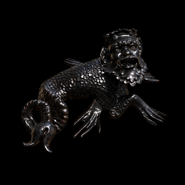 Dark sea monster sculpture with bearded roaring face, scaled body, webbed limbs and knotted forked tail