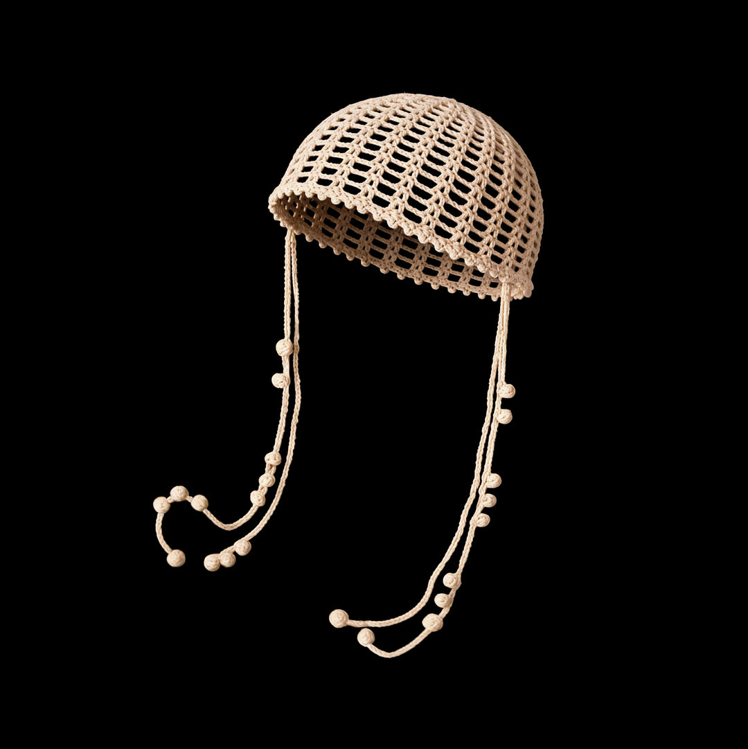 Warm cream open crochet cap with long beaded ties floating against black